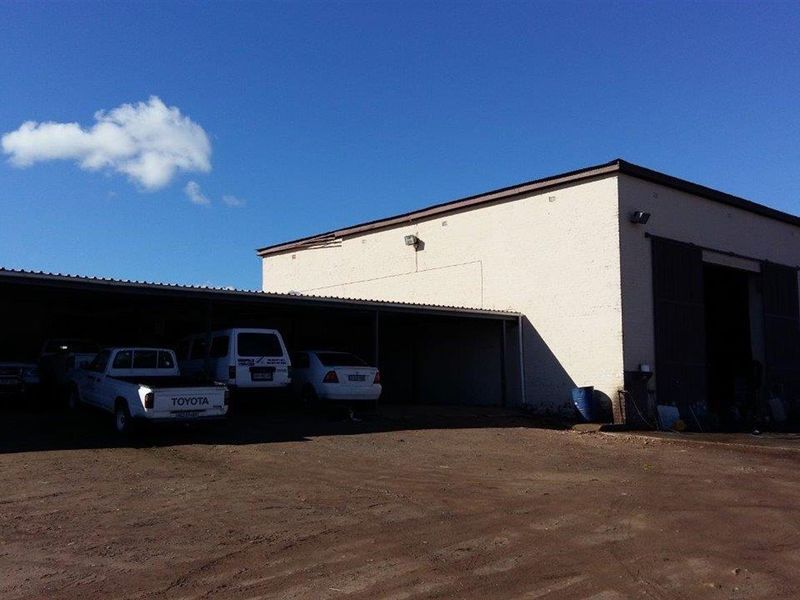 Exterior view of a farm building featuring a large covered parking area and a spacious workshop or storage space with a sliding door.
