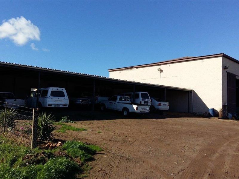 A large covered parking structure on a farm property, featuring a metal roof and steel support columns, suitable for multiple vehicles.