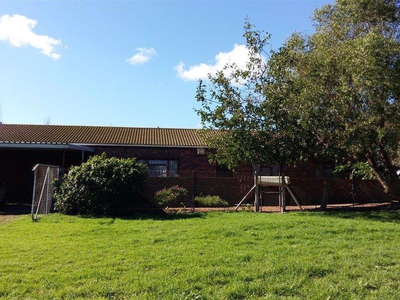 Rear view of a brick farm dwelling featuring a tiled roof, attached carport, and surrounding chain link fencing set within a grassy yard.