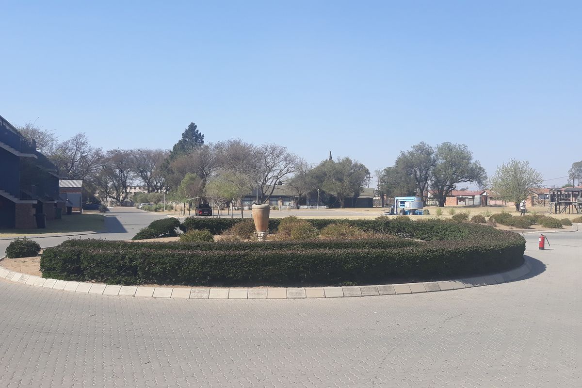 A view of the complex grounds featuring a paved circular driveway, landscaped garden beds, and surrounding residential building blocks.