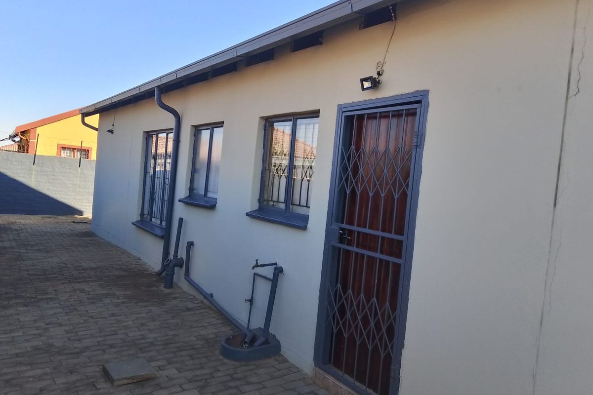 Rear exterior view of the property featuring a paved walkway, security gate, and external wall finishes.