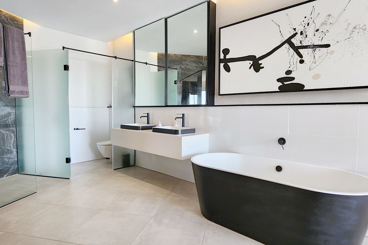 Modern luxury bathroom featuring a freestanding black bathtub, double vanity with vessel sinks, large mirrors, and a spacious walk-in glass shower.