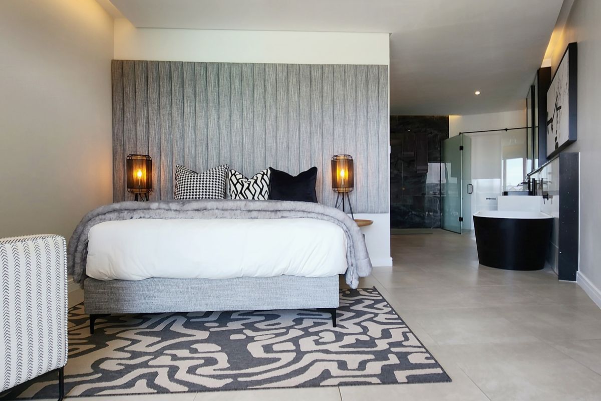 Spacious master bedroom suite featuring a textured feature wall, integrated lighting, and an open-plan en-suite bathroom with a modern freestanding bathtub.