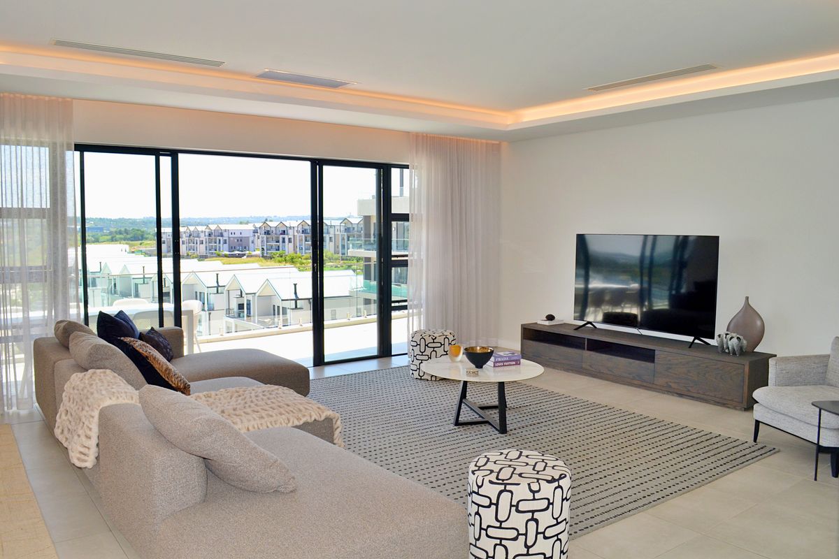 Spacious modern living room featuring recessed ceiling lighting, large sliding glass doors, and seamless access to a private balcony with expansive neighbourhood views.