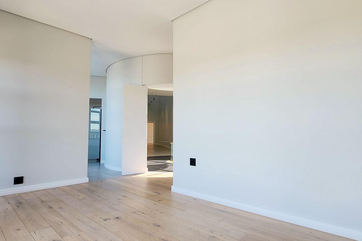 A bright, modern interior space featuring light oak timber flooring, clean white walls, and a unique curved architectural wall element.