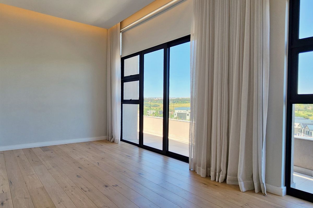 Bright and spacious bedroom featuring light wood flooring, recessed ceiling lighting, and large floor-to-ceiling sliding glass doors opening onto a private balcony.