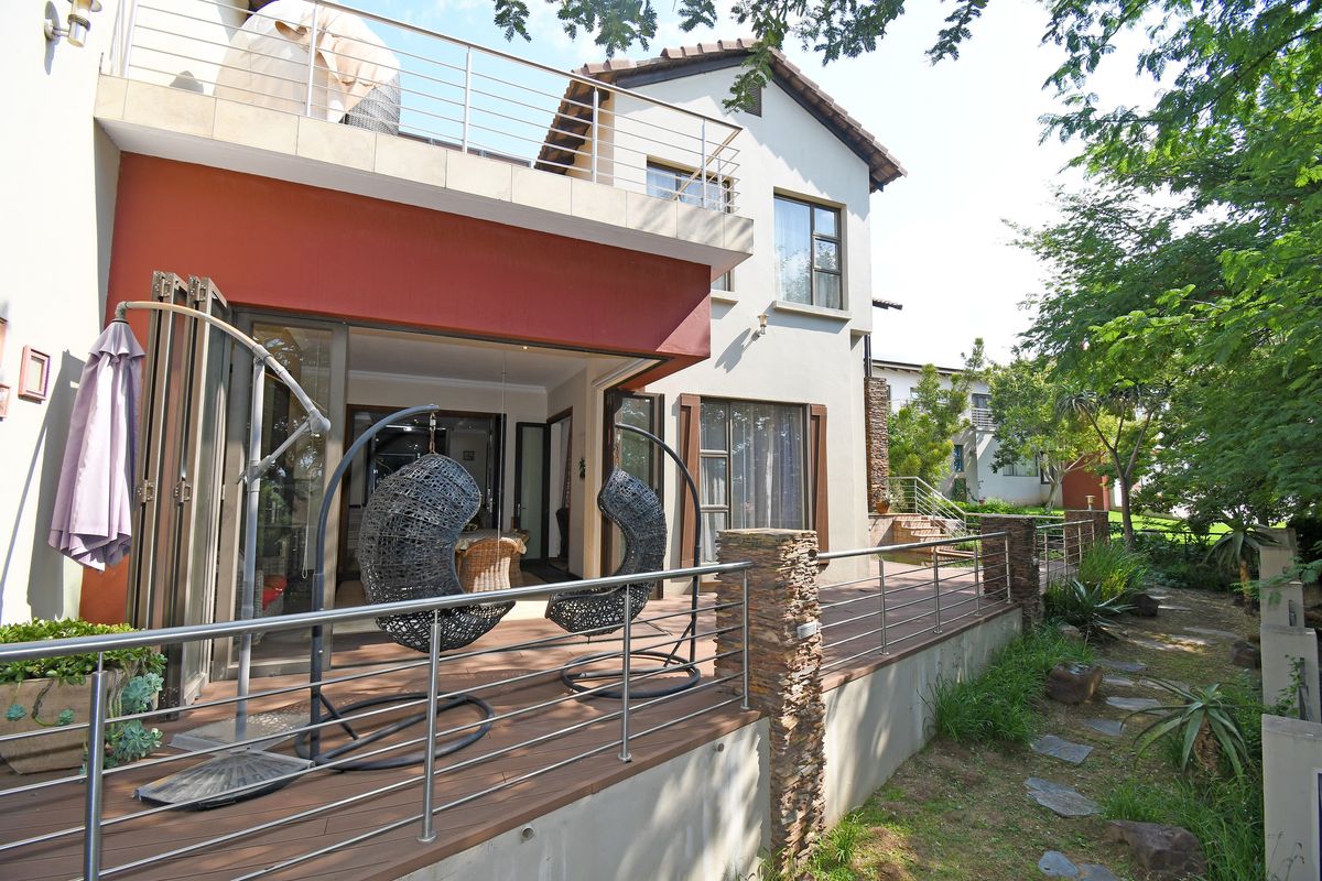 A spacious rear patio featuring composite decking, stainless steel balustrades, and stone-clad pillars, providing seamless indoor-outdoor flow through large sliding glass doors.
