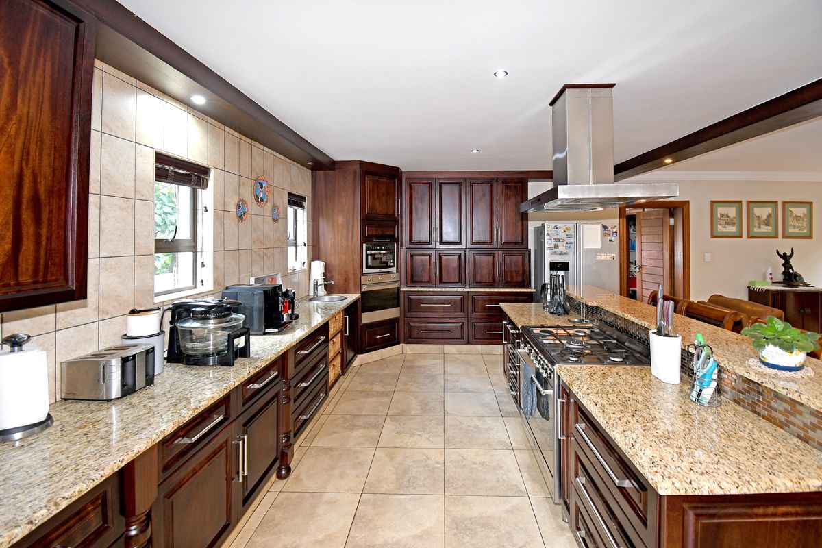 Spacious kitchen featuring dark wood cabinetry, granite countertops, a central island with a gas hob, and stainless steel extractor fan.