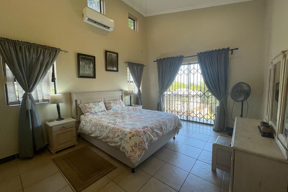 Spacious bedroom featuring high ceilings, tiled flooring, a wall-mounted air conditioner, and a security gate leading to an outdoor area.