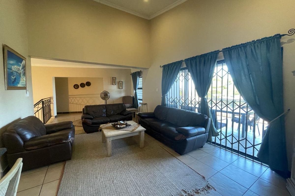 Spacious living room with high ceilings, tiled flooring, and large sliding glass doors leading to an outdoor area, secured with metal security gates.