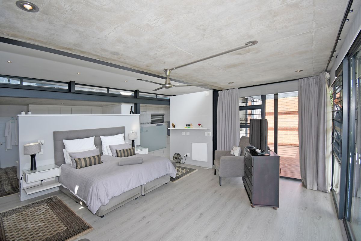 Spacious modern bedroom featuring an exposed concrete ceiling, ceiling fan, and large sliding glass doors opening onto an outdoor deck area.