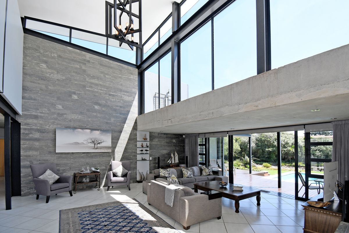 Spacious double-volume living area featuring floor-to-ceiling glass walls, exposed concrete beams, and seamless indoor-outdoor flow to the patio and pool area.