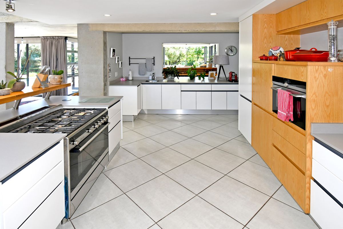 Modern kitchen featuring sleek white cabinetry, light wood paneling, a large gas range, and tiled flooring with an open-plan layout.