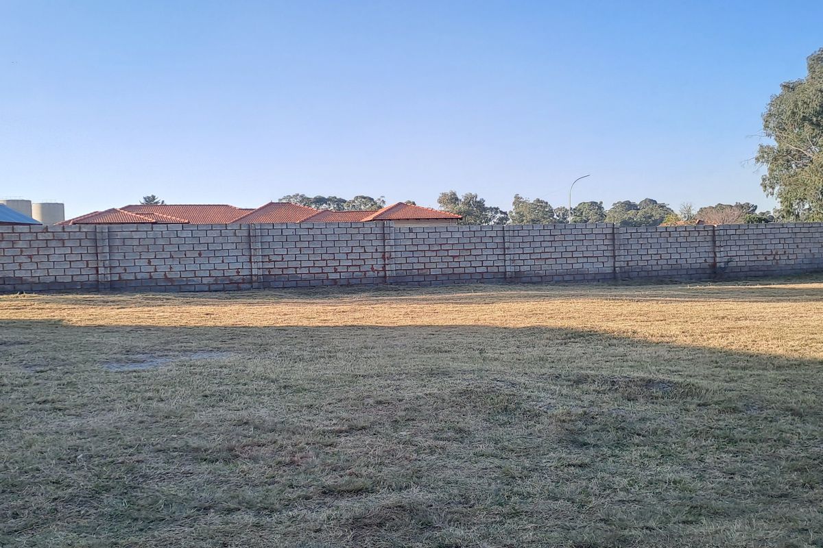 A vacant residential plot featuring a clear, level grass area enclosed by a perimeter boundary wall.
