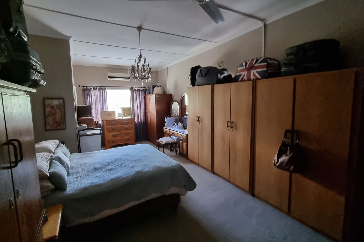 Spacious bedroom featuring extensive built-in wooden cabinetry, a ceiling fan, and a wall-mounted air conditioning unit.