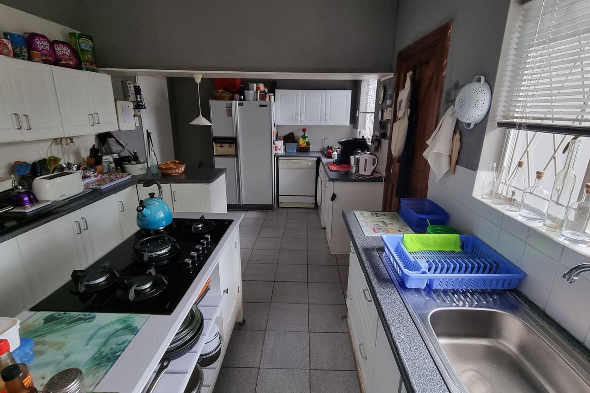 Functional kitchen featuring white cabinetry, a central island with a gas hob, tiled flooring, and a stainless steel sink with a window view.