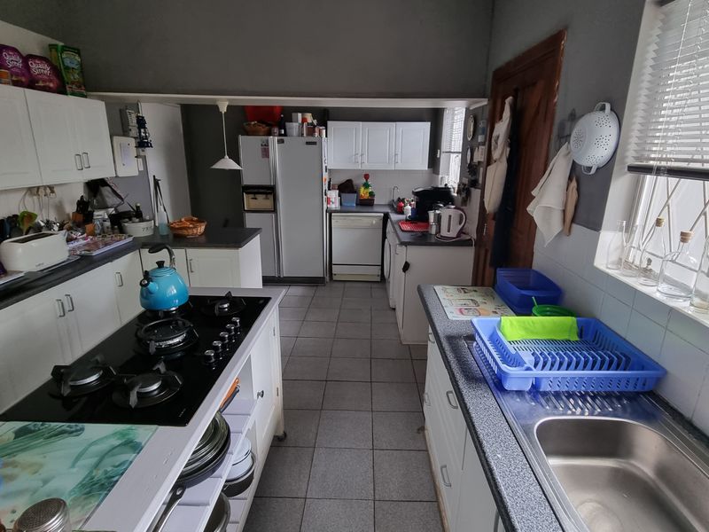 Functional kitchen featuring white cabinetry, a central island with a gas hob, tiled flooring, and a stainless steel sink with a window view.