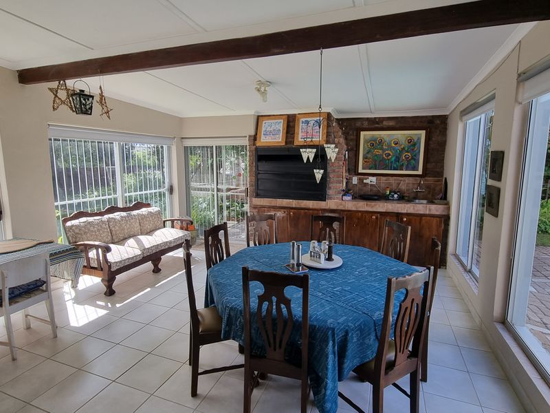 Spacious open-plan living and dining area featuring tiled floors, exposed timber beams, and a built-in braai, with large sliding doors providing garden access.