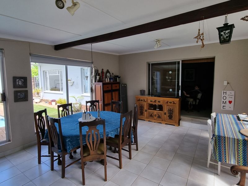 Spacious open-plan living and dining area featuring tiled floors, exposed timber ceiling beams, and large sliding glass doors providing direct access to the pool area.
