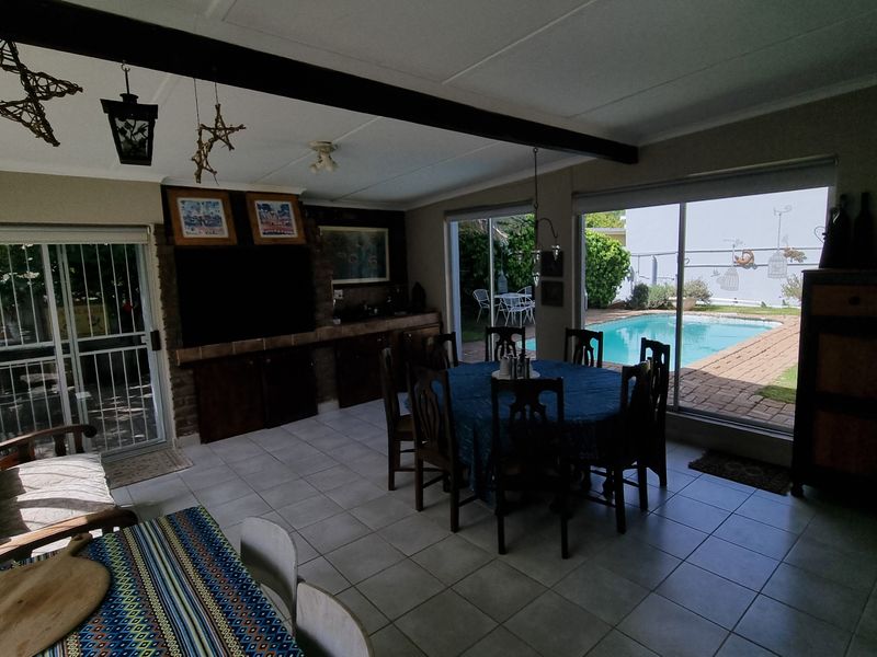 Spacious open-plan living and dining area featuring tiled floors, exposed ceiling beams, and large sliding doors providing direct access to the pool area.