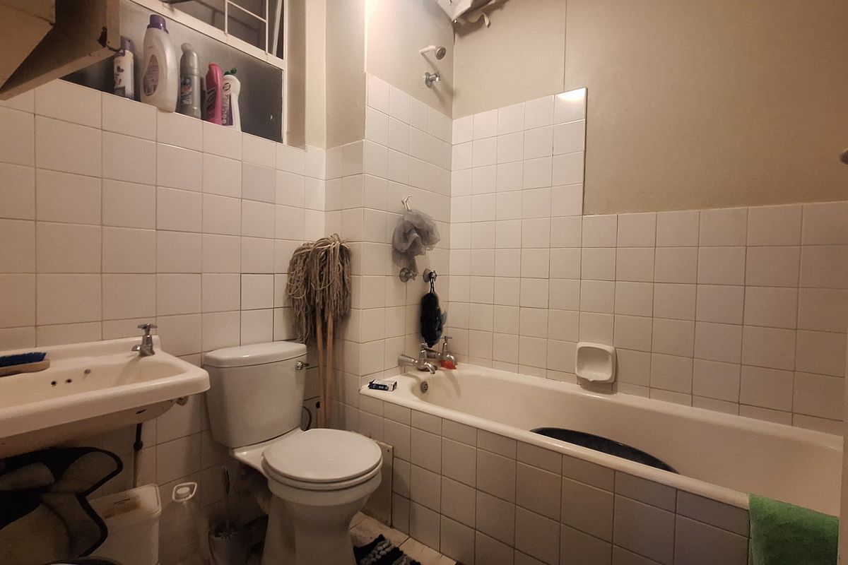 A functional bathroom featuring a bathtub, pedestal basin, and toilet, with white wall tiling. The space would benefit from cosmetic updates and repairs.