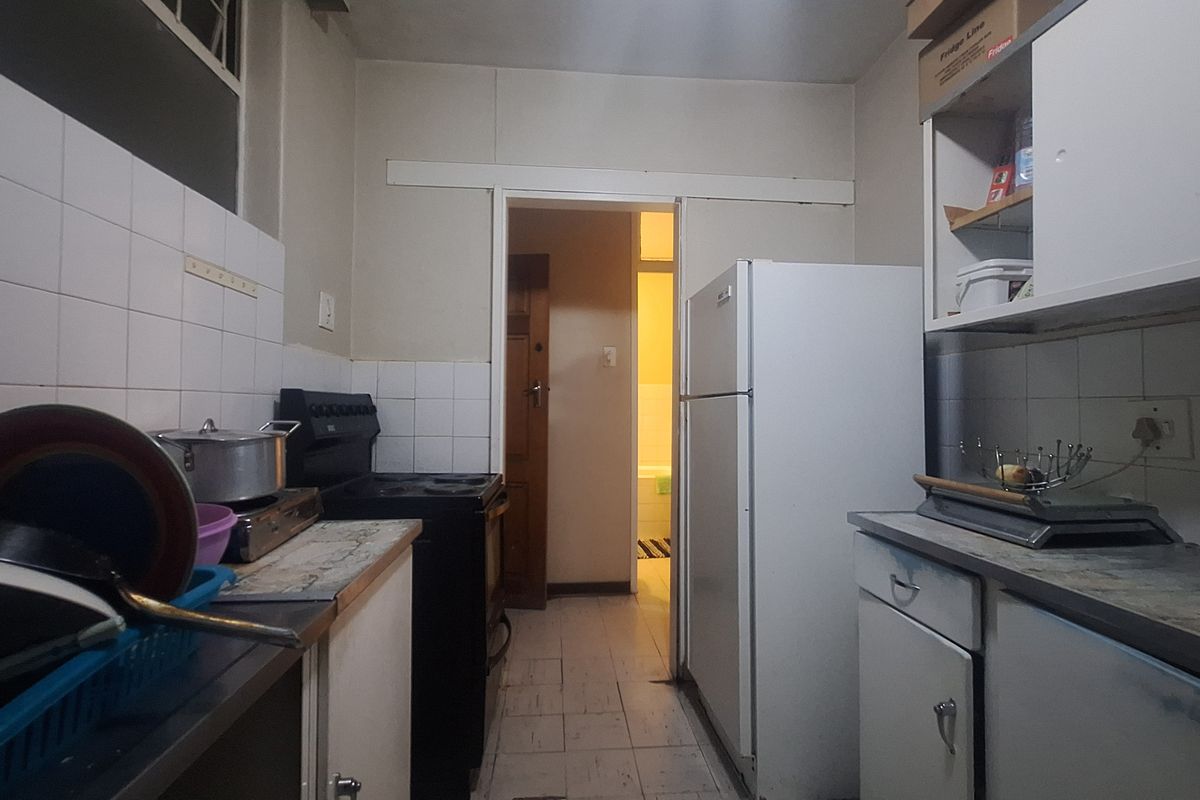 A compact, dated kitchen featuring tiled splashbacks, laminate countertops, and basic cabinetry, offering potential for a modern renovation.
