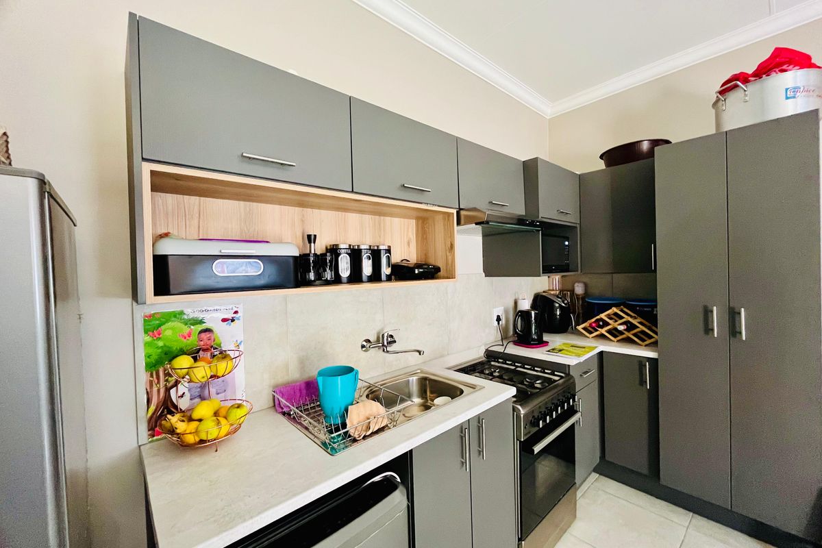 Modern kitchen featuring grey cabinetry, light-toned countertops, a built-in gas stove with extractor fan, and tiled flooring.