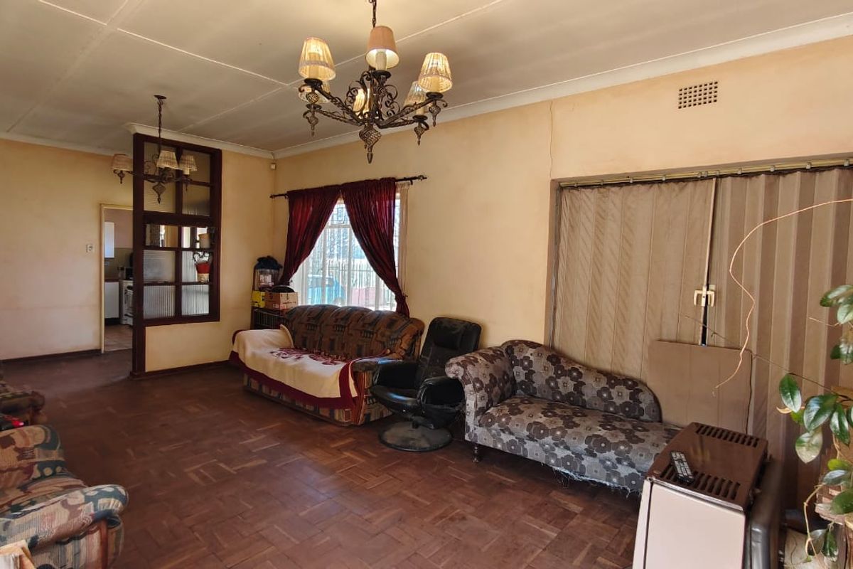Spacious living room featuring original parquet flooring, a decorative chandelier, and a room divider with glass paneling leading to the kitchen area.