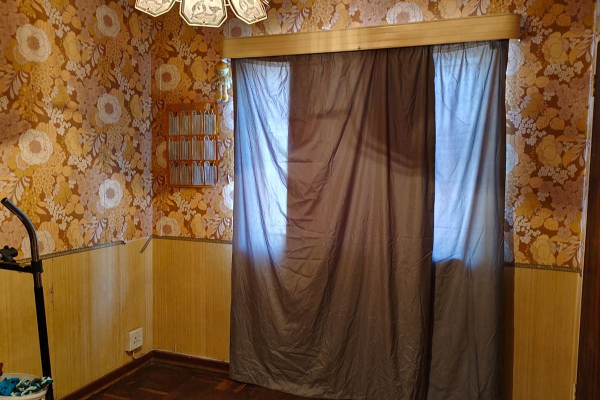 A bedroom featuring vintage floral wallpaper, wood paneling, and dark timber flooring, offering a dated aesthetic ready for modernization.