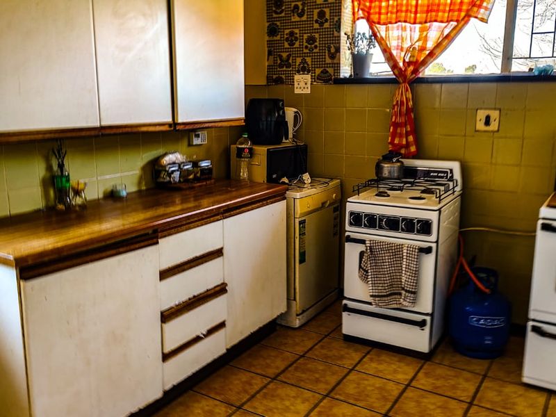A dated kitchen featuring original cabinetry, tiled walls, and tiled flooring, providing a functional space with potential for modernization.