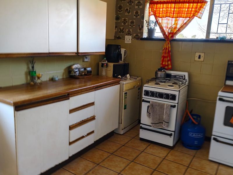 A dated kitchen featuring original cabinetry, tiled splashbacks, and tiled flooring, offering a functional layout with potential for modernization.