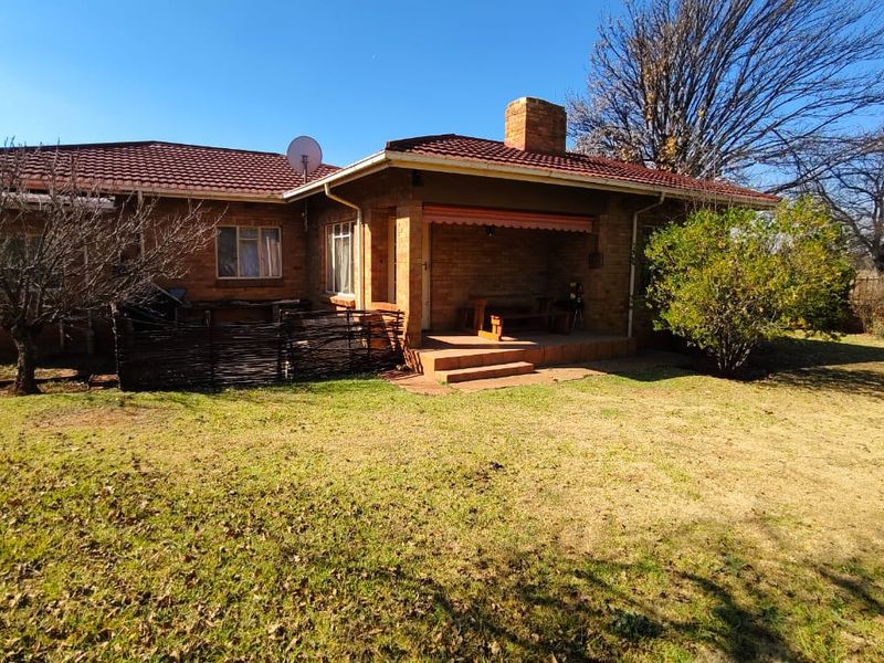 Rear view of a single-story brick house featuring a covered patio area, tiled roof, and a spacious garden.