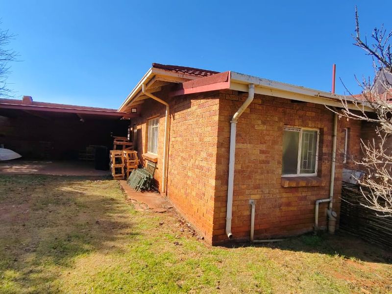 A rear view of a brick house featuring a covered patio area, tiled roof, and a surrounding garden space.