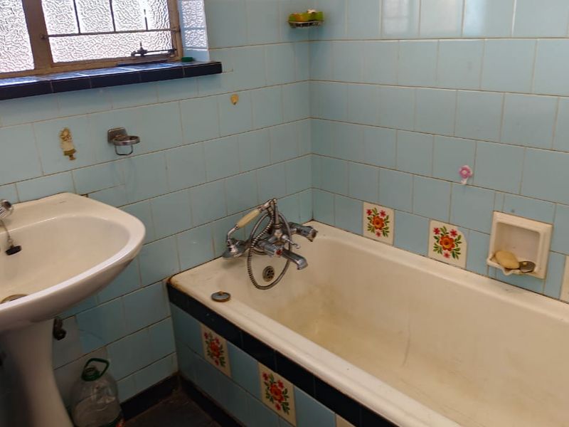 A dated bathroom featuring light blue wall tiles with decorative floral accents, a pedestal basin, and a standard bathtub with vintage-style chrome mixer taps.