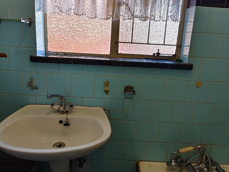 A dated bathroom featuring original blue wall tiles, a pedestal basin, and a window with security bars.