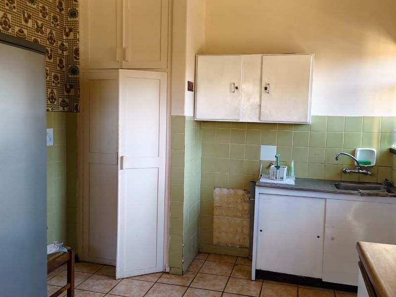 A dated kitchen featuring built-in cabinetry, a single basin sink, and tiled splashbacks, offering potential for a modern renovation.