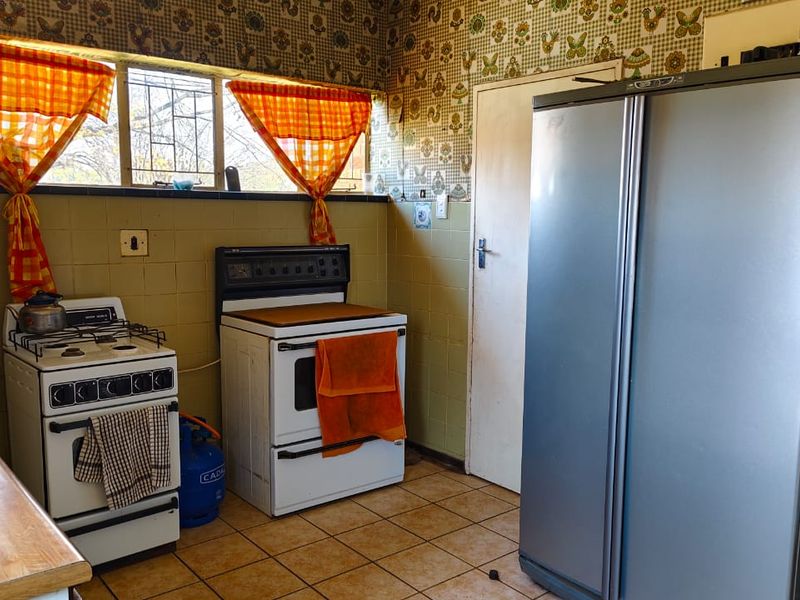 A dated kitchen featuring tiled walls, patterned wallpaper, and functional cooking appliances, offering significant potential for a modern renovation.