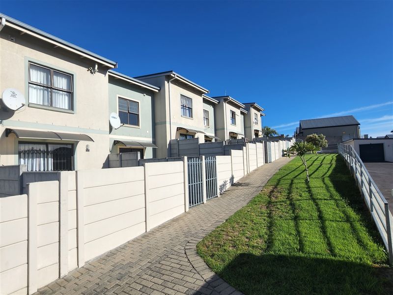 Rear view of the townhouse complex featuring a paved walkway, manicured lawn, and private boundary walls for each unit.