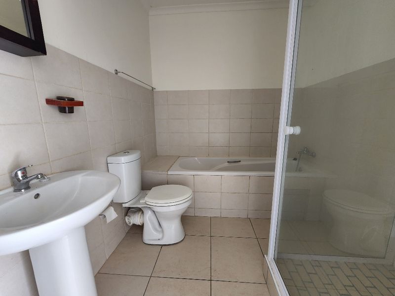 A functional bathroom featuring a pedestal basin, toilet, built-in bathtub, and a separate shower enclosure with tiled finishes.