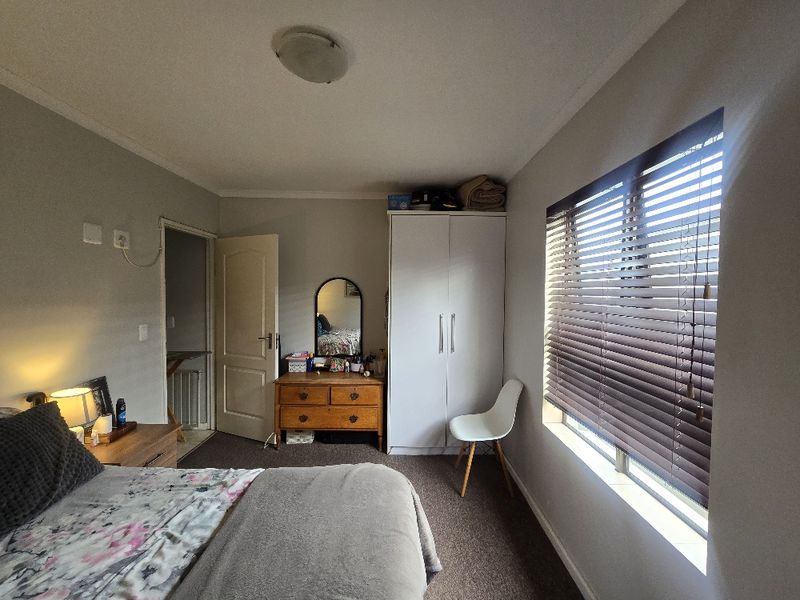 A functional bedroom featuring a built-in wardrobe, venetian blinds, and neutral wall finishes, providing a comfortable and practical living space.