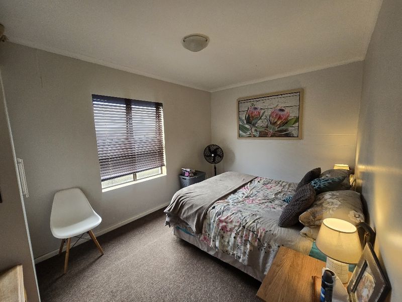 A functional bedroom featuring carpeted flooring, a built-in cupboard, and a window fitted with venetian blinds.