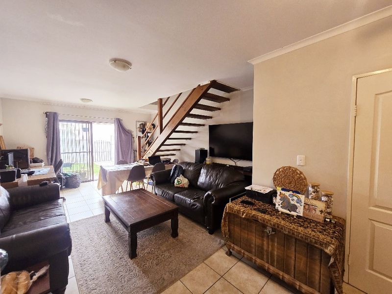 Open plan living area featuring tiled flooring and a wooden staircase leading to the upper level, with direct access to the rear patio.