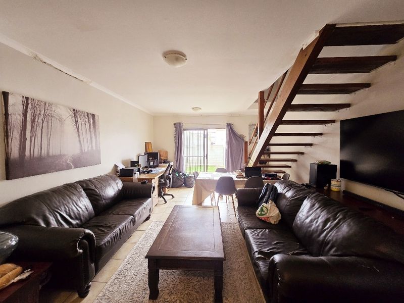 Open-plan living area featuring an exposed staircase, tiled flooring, and sliding door access to the rear exterior.