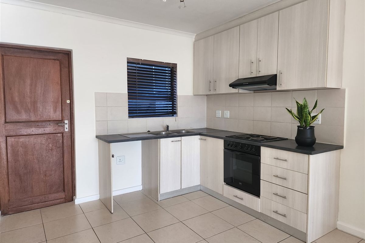 A functional kitchen featuring light wood-grain cabinetry, dark countertops, built-in oven and hob, tiled backsplash, and neutral floor tiles.