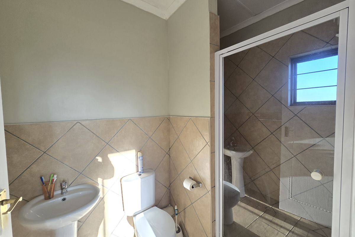 A functional bathroom featuring a pedestal washbasin, toilet, and a separate shower enclosure with tiled finishes throughout.