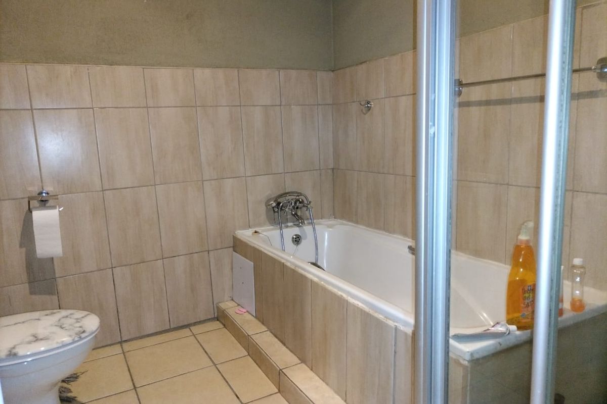 A functional bathroom featuring a built-in bathtub, a separate shower enclosure, and a toilet, finished with neutral wall and floor tiling.