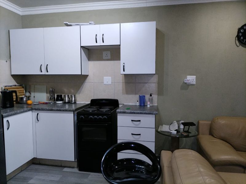 Compact open-plan kitchen featuring white cabinetry, tiled backsplash, and a freestanding electric stove, seamlessly integrated with the adjacent living area.