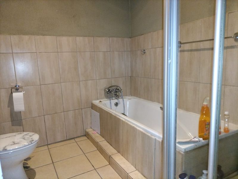 A functional bathroom featuring a built-in bathtub, a separate shower enclosure, and a toilet, finished with neutral wall and floor tiling.