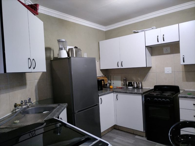 A functional kitchen featuring white cabinetry, tiled backsplash, laminate countertops, and a built-in electric stove with a stainless steel sink.
