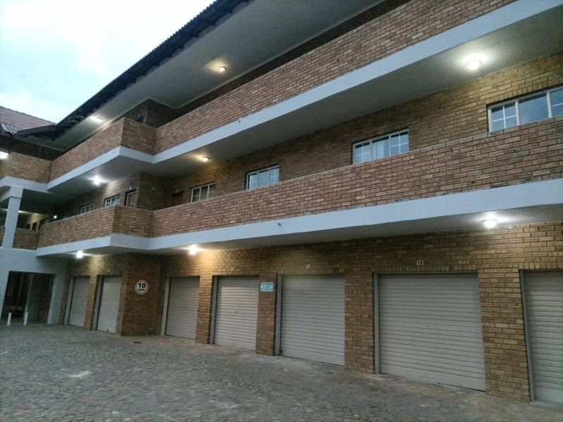 Exterior view of a multi-story apartment complex featuring face brick construction, multiple roller shutter garage doors, and private balconies.